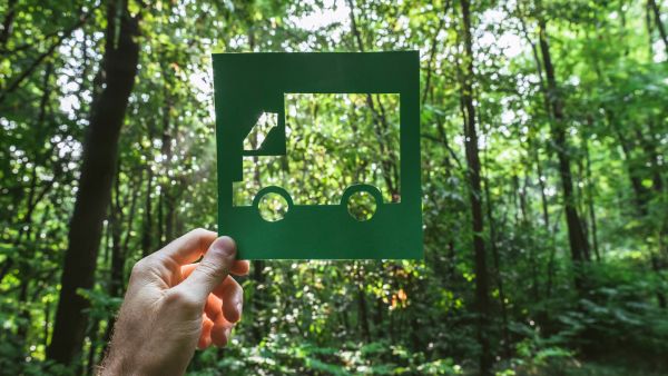 Pessoa segurando cartão com desenho de caminhão em meio às árvores representando a logística sustentável