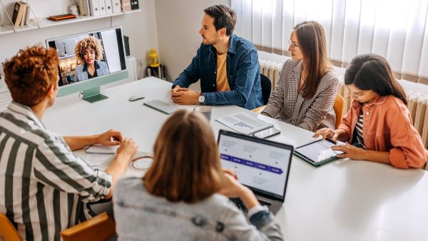 Reunião com membros da equipe no escritório e outro trabalhando remotamente representando modelo híbrido