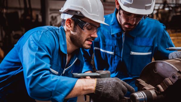 Dois colaboradores operando máquina em conjunto em ambiente de trabalho saudável e que segue o ESG